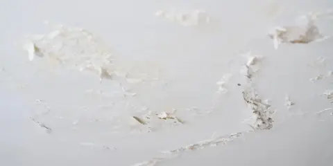 Détails d'un plafond abîmé, avec des morceaux de peinture écaillée révélant le plâtre sous-jacent, signe de salpêtre sur le mur.