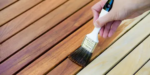Application d'une lasure sur des lattes de bois. La différence entre lasure et peinture est visible : la lasure laisse le grain du bois apparent.