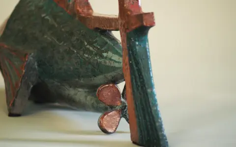 Sculpture de poisson en céramique, style Jean Derval, aux couleurs vives bleu-vert et rouge, avec une hélice visible.