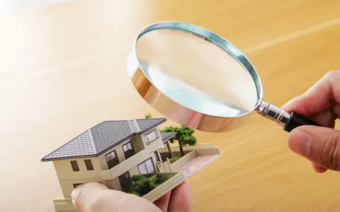 Main tenant examine un modèle de maison avec une loupe pour expertiser un tableau.