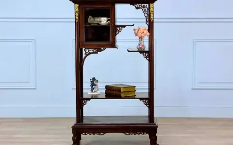 Étagère en bois sombre ornée de motifs dorés, rappelant le style de Gabriel Viardot. Elle présente des tasses dans une vitrine, des livres et des fleurs.