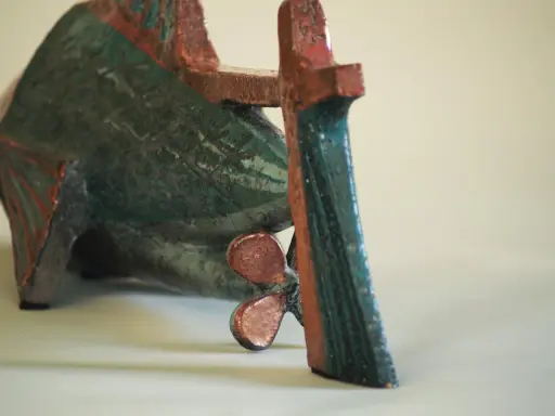 Sculpture de poisson en céramique, style Jean Derval, aux couleurs vives bleu-vert et rouge, avec une hélice visible.