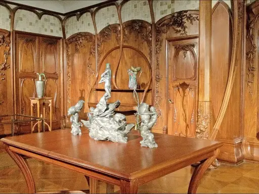 Intérieur Art Nouveau orné de boiseries sculptées, avec une table en bois et des sculptures, évoquant l'œuvre d'Alexandre Charpentier.
