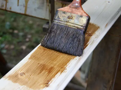 Pinceau appliquant une lasure sur une planche de bois clair, montrant la facilité de lasurer sans poncer pour une finition rapide et efficace.