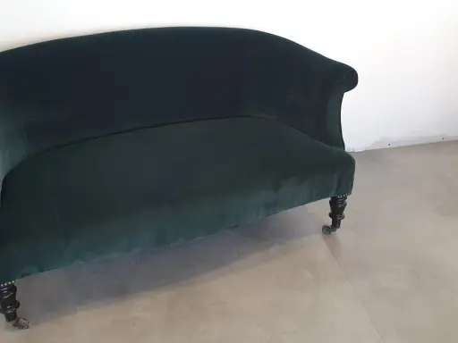 Banquette Napoléon III en velours vert profond, aux pieds sculptés et roulettes. Un meuble élégant pour un salon d'époque.