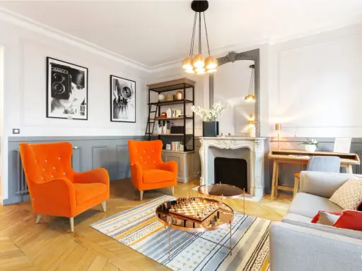 Salon aux fauteuils orange vif, cheminée ornée, et un jeu d'échecs sur table basse, évoquant un mouvement baroque moderne.