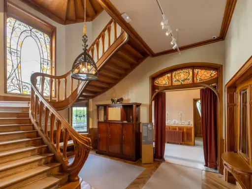 Escalier majestueux en bois, vitraux colorés, mobilier ancien. Un intérieur d'une élégance intemporelle, évoquant le style Majorelle.