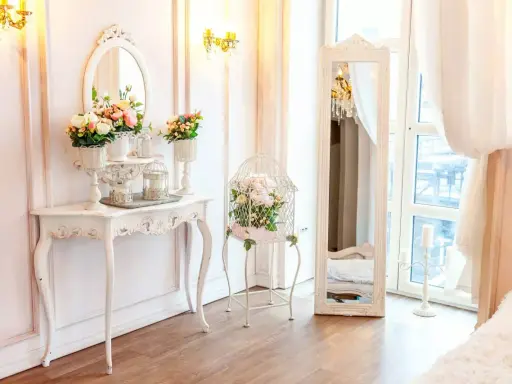 Un boudoir romantique dans un style baroque, avec une console ornée de fleurs, une cage à oiseaux décorative et un grand miroir.