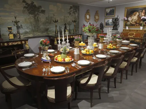 Table dressée dans un style directoire, avec fruits, fleurs et vaisselle raffinée. Le décor mural évoque un paysage champêtre.