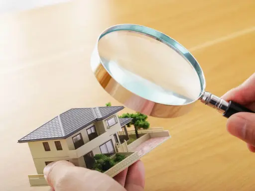 Main tenant examine un modèle de maison avec une loupe pour expertiser un tableau.