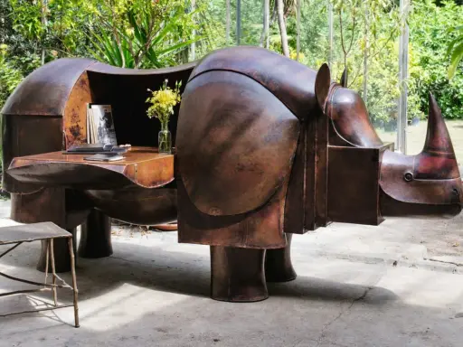 Étonnante sculpture lalanne en forme de rhinocéros, bureau fonctionnel en cuivre patiné, avec un vase de fleurs jaunes et une chaise en métal.