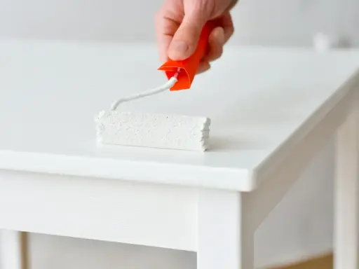 Main blanche d'un meuble laqué, un rouleau de peinture blanc est appliqué.