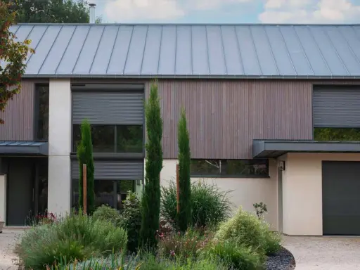 Façade moderne avec volet roulant maison ancienne, bois, pierre et jardin luxuriant.