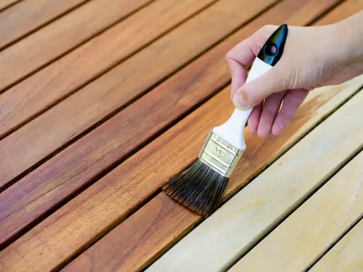 Application d'une lasure sur des lattes de bois. La différence entre lasure et peinture est visible : la lasure laisse le grain du bois apparent.