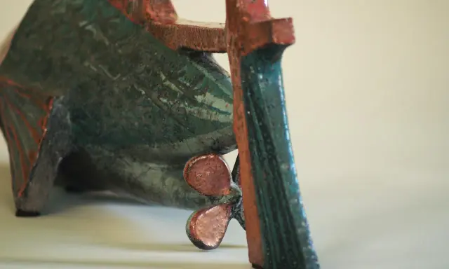 Sculpture de poisson en céramique, style Jean Derval, aux couleurs vives bleu-vert et rouge, avec une hélice visible.