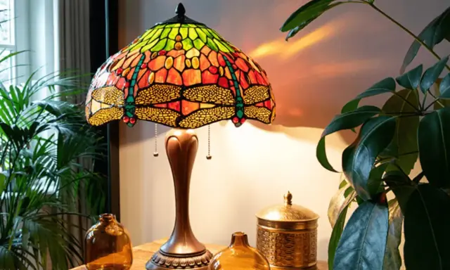 Lampe tiffany origine, avec abat-jour en vitrail coloré orné de libellules, posée sur une table en bois près de plantes vertes.