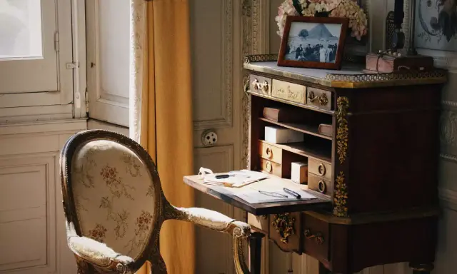 Bureau secrétaire ancien, fauteuil fleuri. Un tableau et des fleurs ornent le dessus. Idéal pour un coût inventaire mobilier succession.
