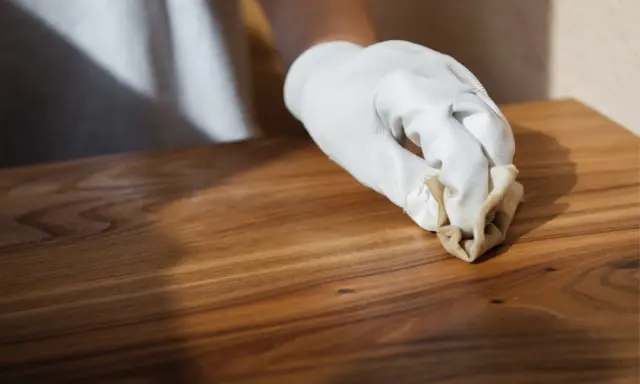 Main d'une personne portant un gant blanc, cirant un meuble en bois après décapage. La cire donne un éclat subtil au bois.