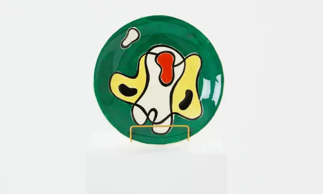 Assiette ronde verte ornée de formes abstraites noires, jaunes, rouges et blanches, dans le style de Roland Brice.