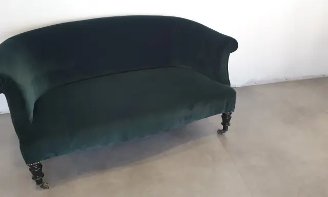 Banquette Napoléon III en velours vert profond, aux pieds sculptés et roulettes. Un meuble élégant pour un salon d'époque.