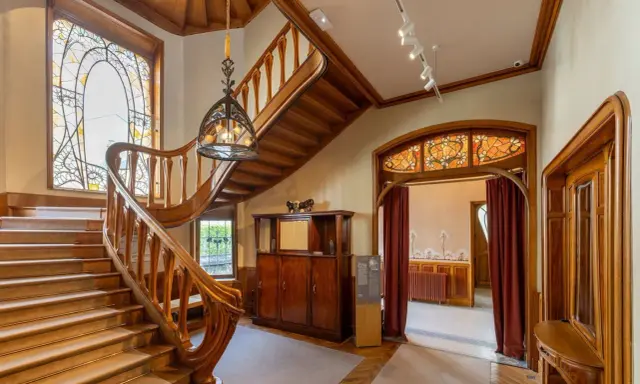 Escalier majestueux en bois, vitraux colorés, mobilier ancien. Un intérieur d'une élégance intemporelle, évoquant le style Majorelle.