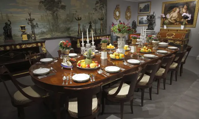 Table dressée dans un style directoire, avec fruits, fleurs et vaisselle raffinée. Le décor mural évoque un paysage champêtre.