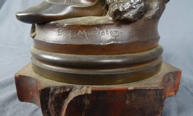 Signature "Eug. Marioton" gravée sur la base d'une sculpture en bronze patiné, posée sur un socle en marbre rouge.