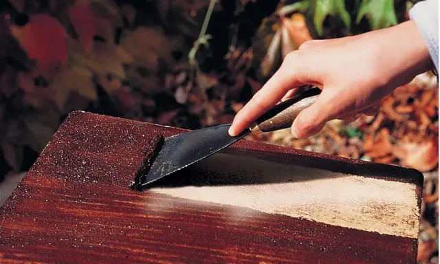 Main d'une personne utilisant un grattoir pour décaper peinture sur bois avec bicarbonate.