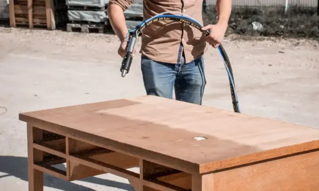 Un homme utilise un appareil pour poncer ou décaper un bureau en bois, révélant une surface plus claire.