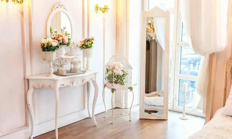 Un boudoir romantique dans un style baroque, avec une console ornée de fleurs, une cage à oiseaux décorative et un grand miroir.