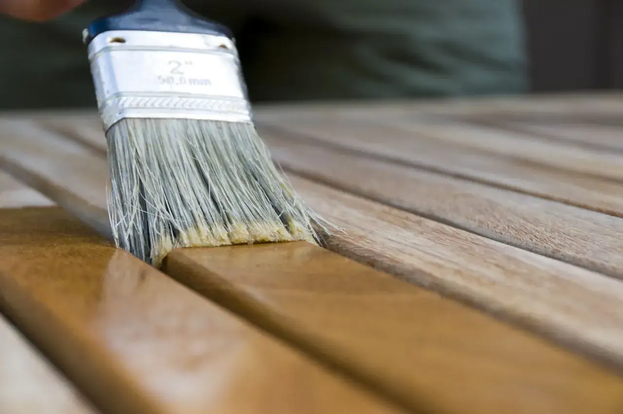 Application d'une finition sur du bois fraîchement poncé. Un pinceau applique une couche protectrice pour nettoyer le bois après ponçage.