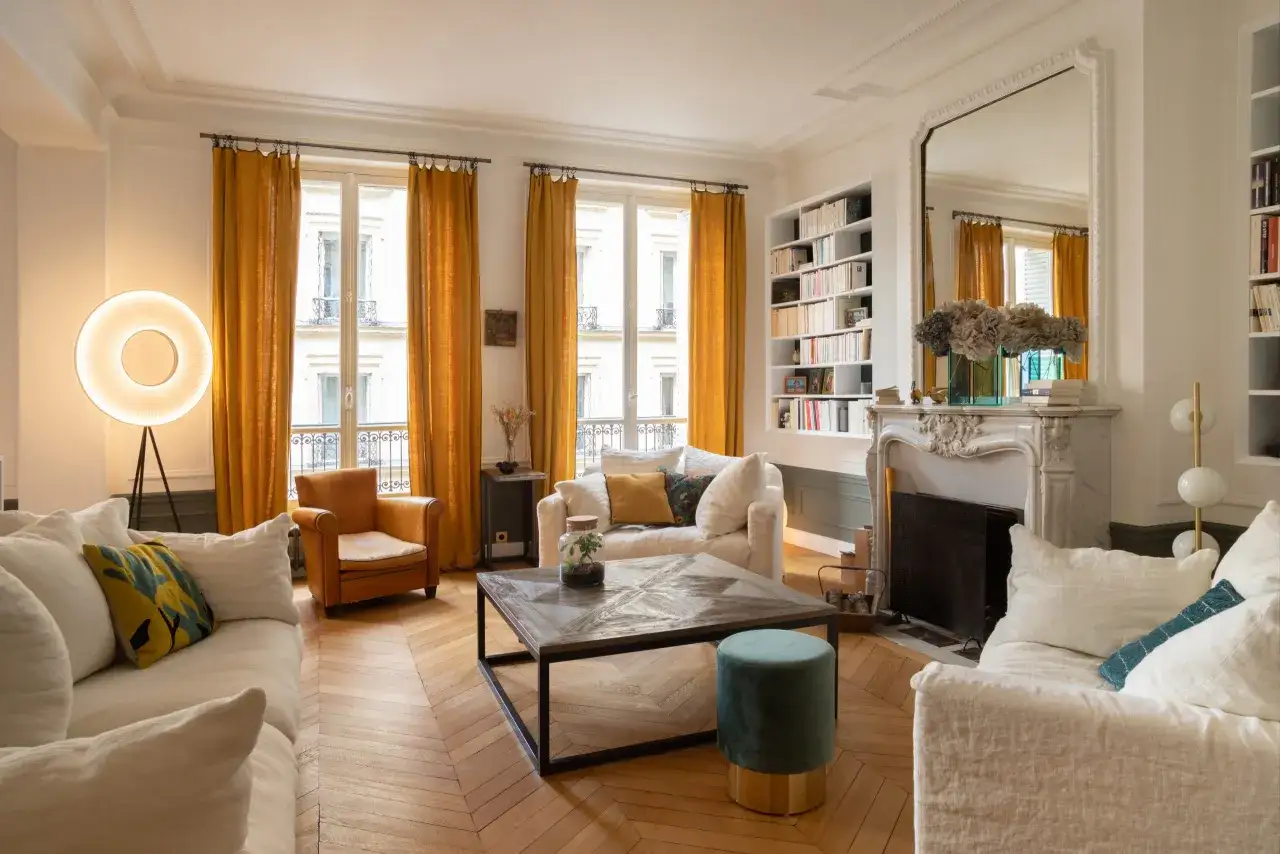 Salon lumineux avec fauteuil en cuir cognac, canapés blancs et rideaux ocre. Quelle couleur avec meuble Louis Philippe ? Le cognac et l'ocre s'harmonisent bien.