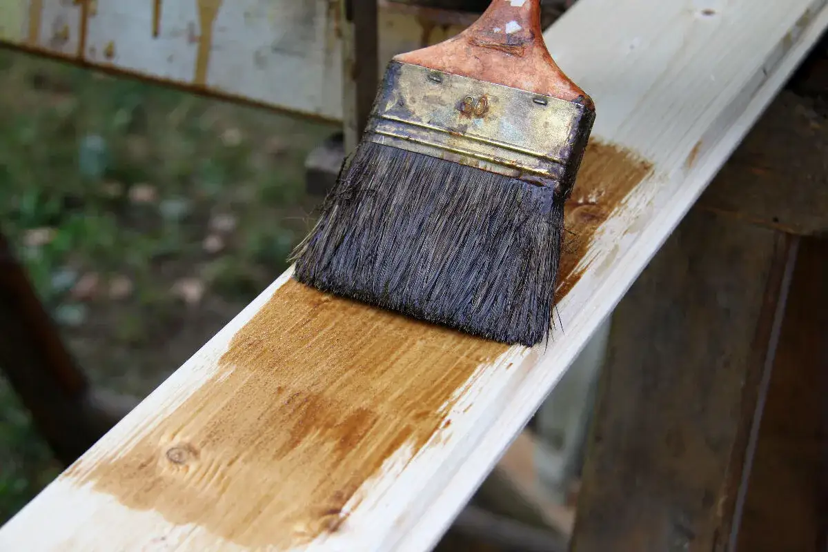 Pinceau appliquant une lasure sur une planche de bois clair, une m&eacute;thode simple pour lasurer sans poncer.