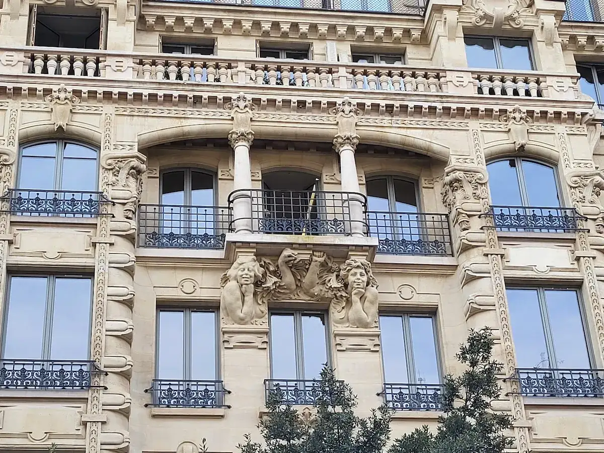 Fa&ccedil;ade d'un immeuble parisien, style restauration architecture, avec balcons en fer forg&eacute; et sculptures de visages.
