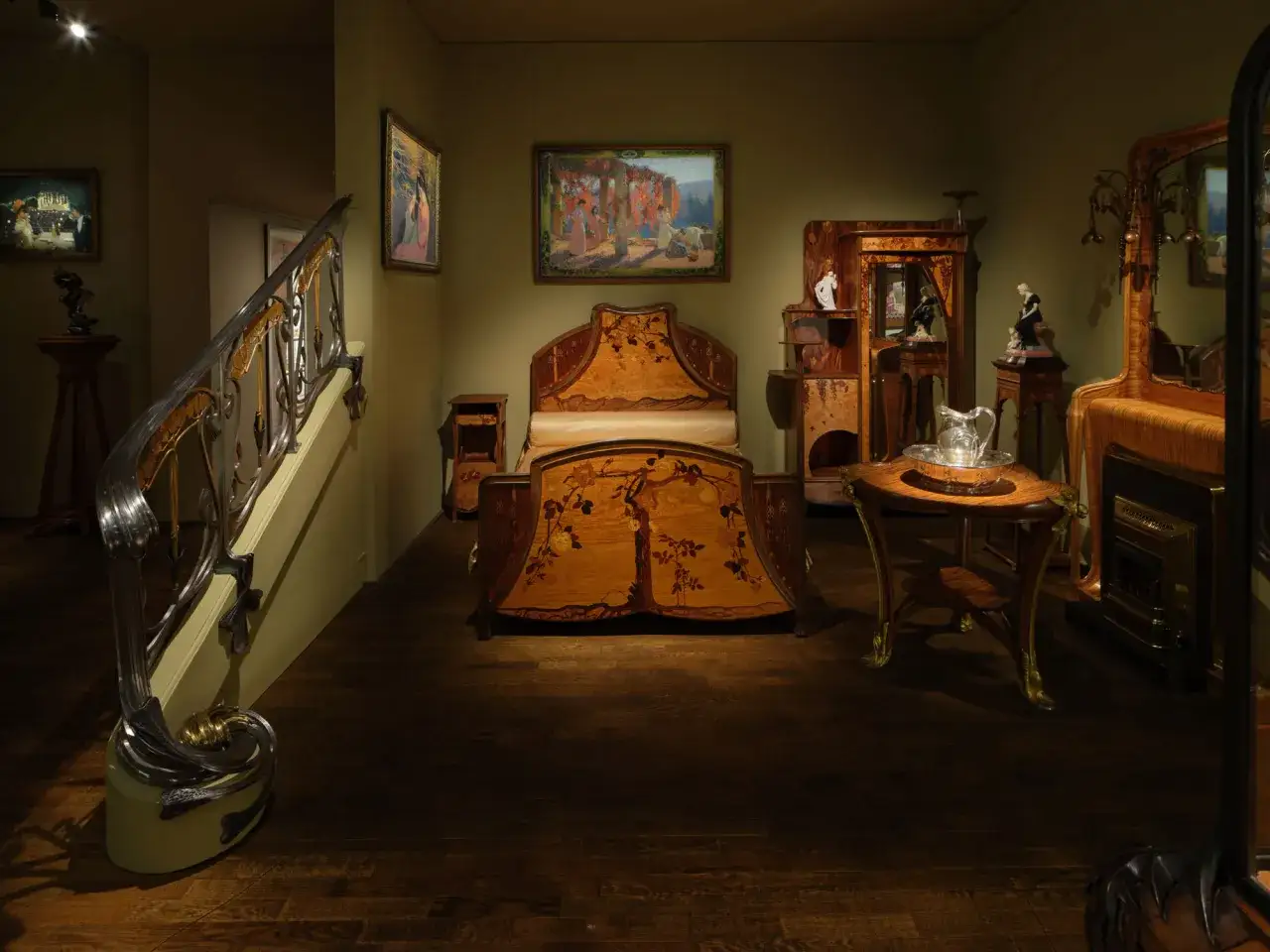 Chambre à coucher d'inspiration art déco, avec un lit orné de marqueterie florale, une armoire sculptée et un escalier majestueux.