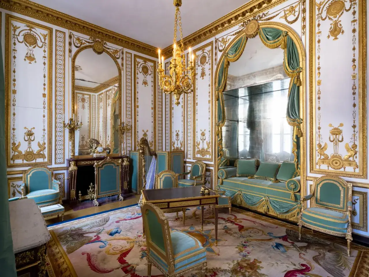 Salon aux boiseries dorées et au mobilier turquoise, évoquant un mouvement baroque. Un tapis orné de motifs floraux et animaliers au sol.