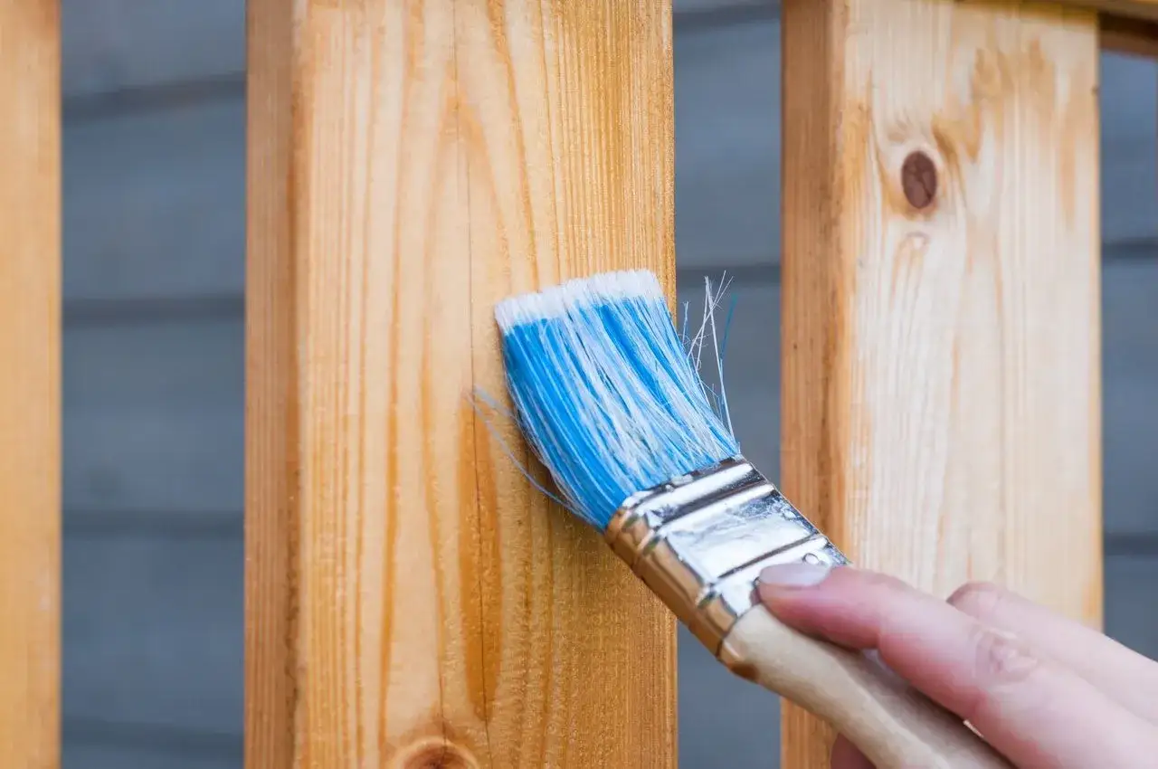 Application d'un produit pour protéger le bois de l'humidité sur une balustrade en bois clair.
