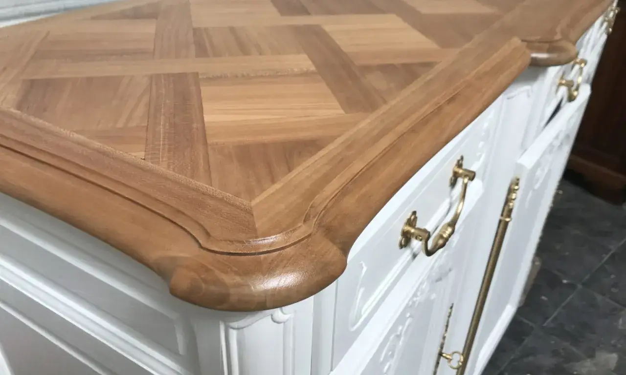 D&eacute;tail d'un meuble blanc avec un plateau en bois &agrave; motif damier. Les poign&eacute;es dor&eacute;es sont visibles, un aper&ccedil;u de comment enlever des ferrures sur un meuble.