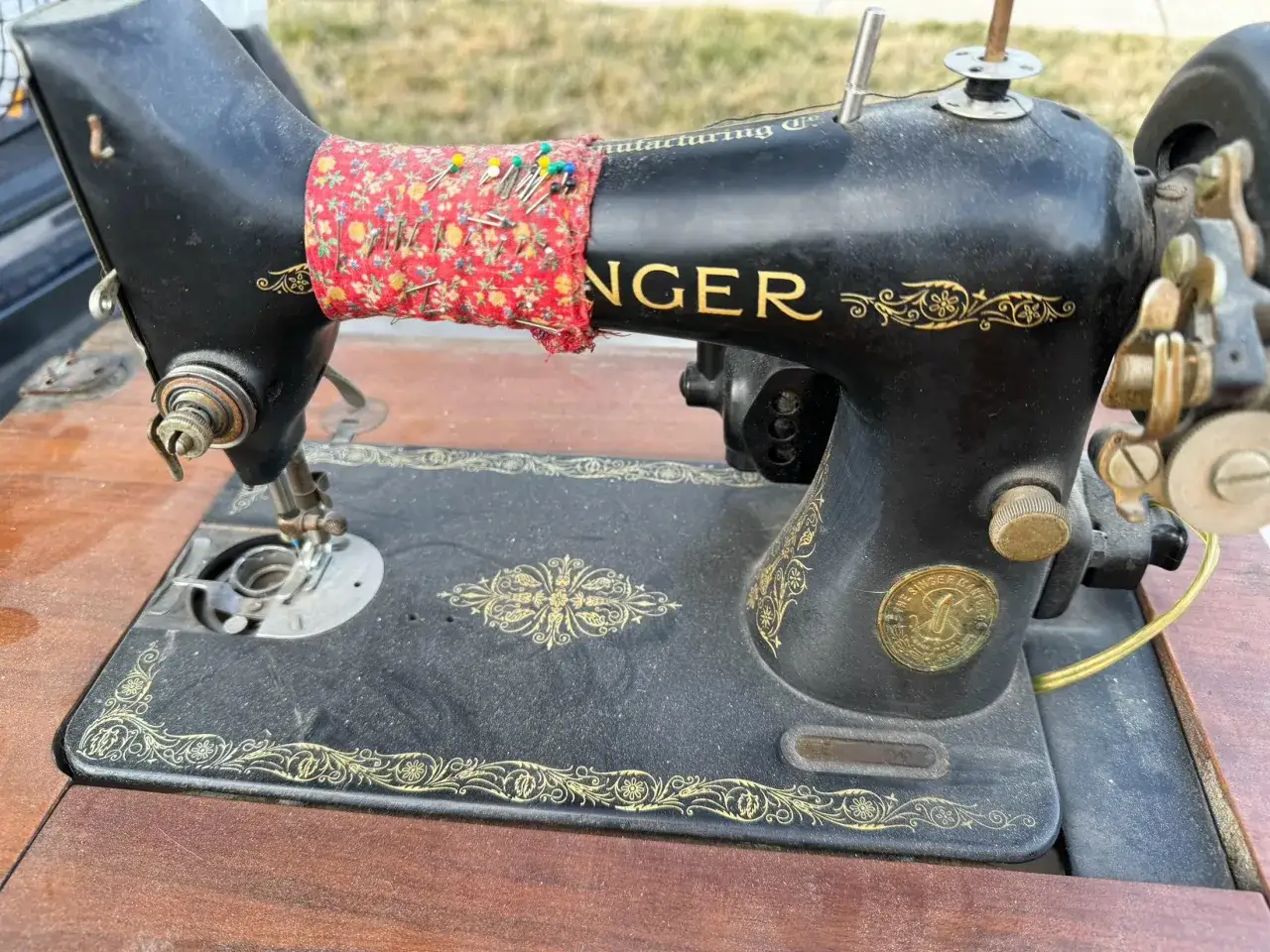 Machine &agrave; coudre Singer ancienne, noire avec d&eacute;corations dor&eacute;es. Un coussin &agrave; &eacute;pingles fleuri est fix&eacute; sur le bras. Estimation possible via le num&eacute;ro de s&eacute;rie.