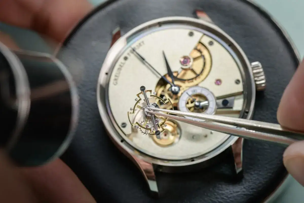 Un horloger assemble un mouvement complexe, d&eacute;montrant son expertise montre. Les rouages dor&eacute;s et les minuscules composants r&eacute;v&egrave;lent un savoir-faire exceptionnel.