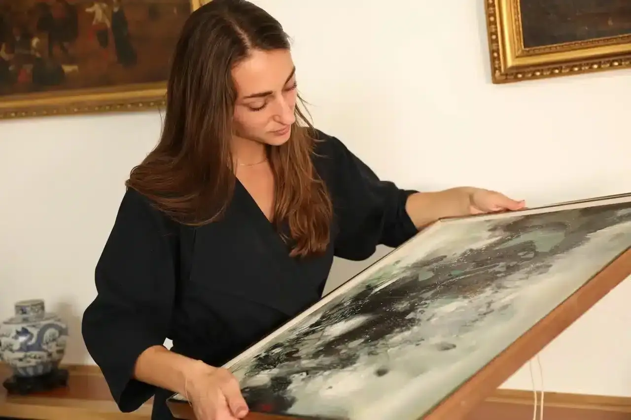Une femme examine un tableau abstrait, cherchant des indices pour comment estimer un tableau avec signature.
