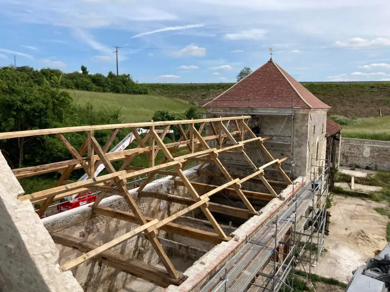 Un chantier de rénovation d'un vieux bâtiment, avec une charpente en vers blanc bois en cours de construction, sous un ciel bleu.