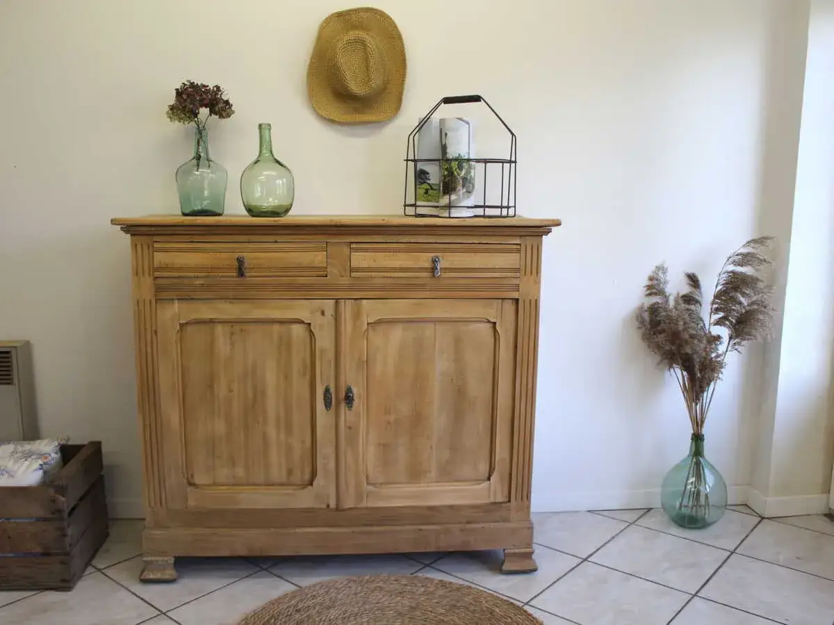 Meuble ancien en bois clair, prêt pour une recette de grand-mère pour décaper un meuble. Décoration champêtre avec des vases en verre et des herbes séchées.