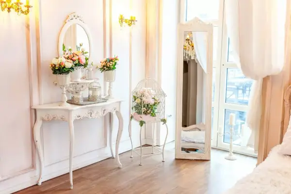 Un boudoir romantique dans un style baroque, avec une console ornée de fleurs, une cage à oiseaux décorative et un grand miroir.