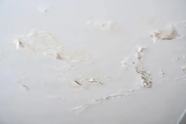 Détails d'un plafond abîmé, avec des morceaux de peinture écaillée révélant le plâtre sous-jacent, signe de salpêtre sur le mur.
