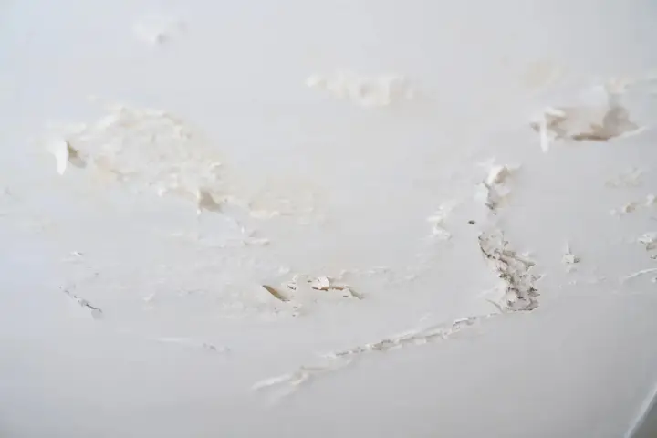 Détails d'un plafond abîmé, avec des morceaux de peinture écaillée révélant le plâtre sous-jacent, signe de salpêtre sur le mur.