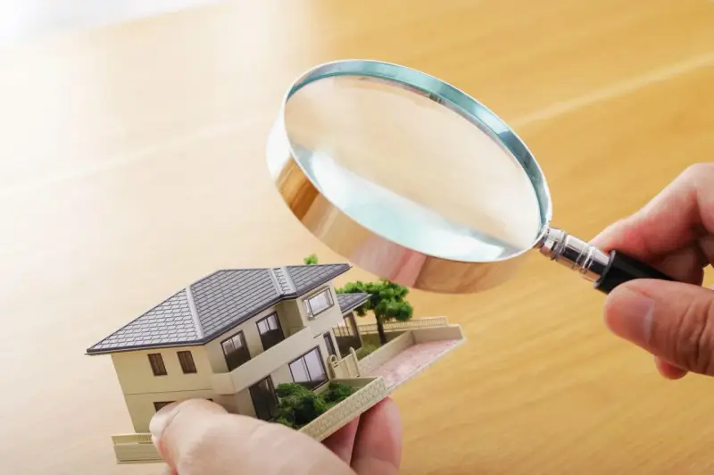 Main tenant examine un modèle de maison avec une loupe pour expertiser un tableau.